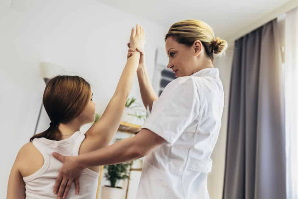 How Can Chiropractic Care Help Shoulder Injuries? Teen Girl having chiropractic back adjustment. Osteopathy, Physiotherapy, Kinesiology. Bad posture correction. Shoulder injuries